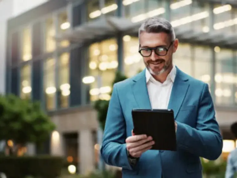 Confident man over 40 in a business suit smiling while working on a tablet outdoors, representing experienced professionals in online business.