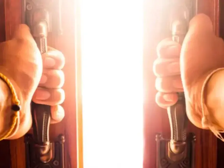 Hands opening ornate wooden doors to reveal a dazzling bright light, symbolizing new opportunities and overcoming fear.
